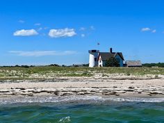 a white house sitting on top of a lush green field next to the ocean in front of a blue sky