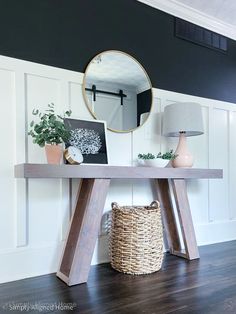 a wooden table with a basket underneath it and a round mirror on the wall behind it