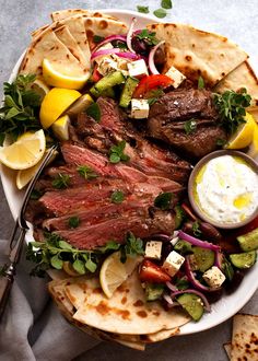 a plate filled with meat, vegetables and pita bread