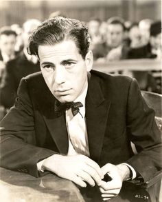 a man in a suit sitting at a table with his hand on his lapel