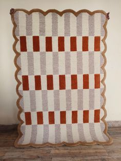 an orange and white checkered quilt on a wooden floor in front of a wall