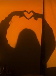 the shadow of a person making a heart shape with their hands in front of an orange wall