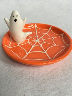 a small white ghost sitting on top of an orange plate with spiderweaves