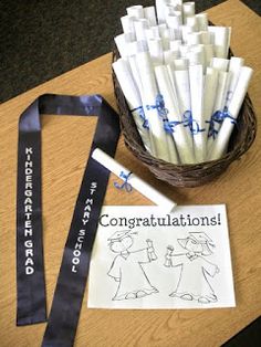 a basket filled with white candles next to a blue ribbon and congratulations sign on top of a wooden table