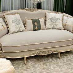 a couch with many pillows on it in front of a chandelier and curtains