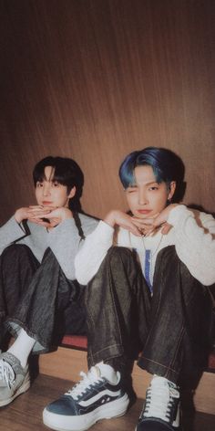 two young men sitting next to each other on top of a wooden floor in front of a wall