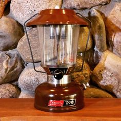 a brown lantern sitting on top of a wooden table next to rocks and a stone wall