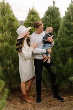 a man and woman holding a baby in their arms while standing next to some trees