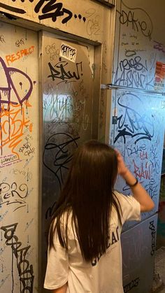 a woman standing in front of a refrigerator covered in graffiti and writing on it's walls