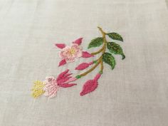 embroidered flowers on white linen with green stems and pink leaves in the center, closeup