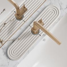 two gold faucets on the side of a white sink with marble counter top