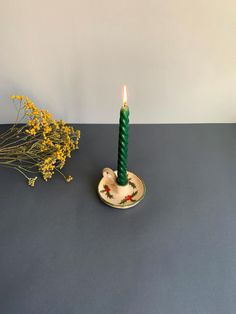 a green candle sitting on top of a table next to yellow flowers and a vase