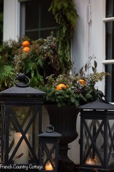 two black lanterns with oranges in them sitting on the ground next to a window