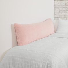 a bed with a pink pillow on top of it next to a white brick wall