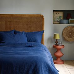 a bed with blue sheets and pillows next to a wicker headboard in a bedroom