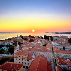 the sun is setting over an old town by the water's edge, with buildings in the foreground