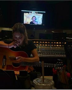 a woman is playing an acoustic guitar in front of the sound board and recording equipment