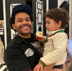 a man holding a little boy in his arms and looking at the cupcake he is holding