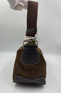 This sought after vintage nylon Tessuto Prada shoulder bag is the perfect 90's accessory. Made from brown nylon, a brown webbing strap, brown leather trim and features silver Prada branded hardware. On the front is the iconic Prada ceramic/metal plaque and inside the bag is lined with the Prada logo lining. There is an interior zipped pocket for valuables. The bag is in overall good vintage condition, some slight scratches can be seen on the leather patches on the bottom corners and the brown ny Brown Nylon Bag With Leather Trim, Brown Nylon Shoulder Bag With Detachable Strap, Classic Brown Nylon Bag, Prada Nylon Bag, 90s Accessories, Vintage Prada, Prada Shoulder Bag, Prada Nylon, Prada Logo