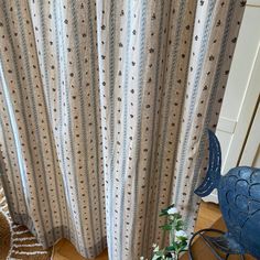 a blue chair sitting in front of a window next to a white and brown curtain