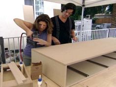 a man and woman standing next to each other in front of a table that is being built