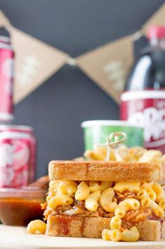 a sandwich with macaroni and cheese on it sitting next to cans of soda