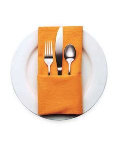 a white plate topped with silverware next to an orange napkin