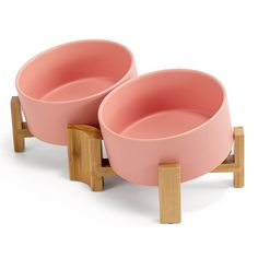 two pink bowls sitting on wooden stands against a white background