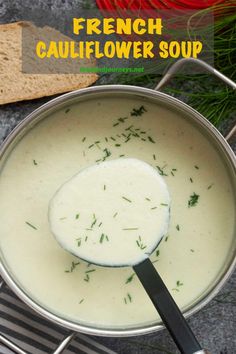 a spoon in a pot filled with white sauce and garnished with fresh herbs