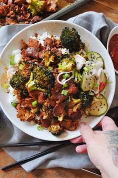 a white plate topped with meat and veggies on top of rice next to chopsticks