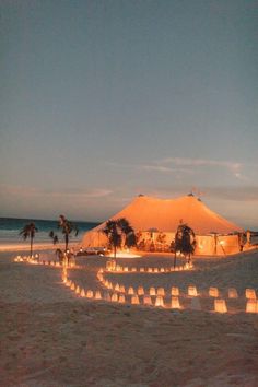 a tent set up on the beach at night with candles lit in front of it