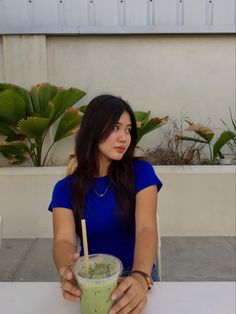 a woman sitting at a table with a drink in her hand and holding a straw