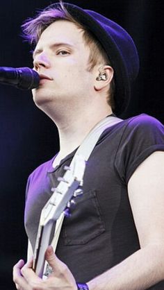 a young man singing into a microphone while wearing a black hat and holding an electric guitar