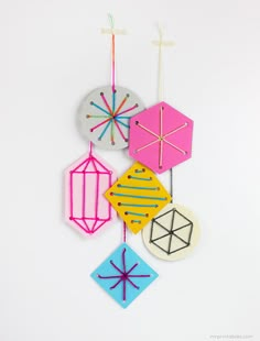 four different colored kites hanging from strings on a white wall in the shape of an ornament