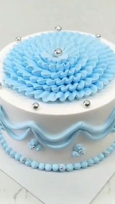 there is a blue and white cake on the table with silver beads around it's edges