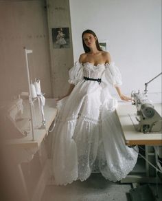 a woman in a white dress is standing on a table with a sewing machine behind her