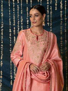 "Jashn-E-Ulfat" - a collection of ensembles that evoke a sense of majestic opulence and modern royalty. Suffused with deep rich hues set on plush cotton silk enhanced with remarkable craftsmanship like Marodi, Mirror and Zardozi embroidery, each ensemble has a romantic and feminine charm of its own collection. This set of 3 consists of a Kurta, Salwar and Dupatta. Kurta: This dainty peach chanderi silk kurta is enhanced with handcrafted zardozi, sitara and zardozi jaal work on the neck, buttas o Luxury Pink Cotton Silk Kurta, Luxury Embroidered Katan Silk Fabric For Eid, Luxury Elegant Silk Thread Dupatta, Luxury Tussar Silk Dupatta With Kora Detailing, Luxury Zari-work Katan Silk Embroidered Fabric, Luxury Katan Silk Fabric With Embroidered Pallu, Ceremonial Sharara With Dabka Work, Formal Art Silk Dupatta With Intricate Embroidery, Festive Peach Anarkali Set With Intricate Embroidery