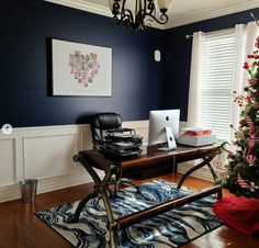 a desk with a computer on top of it in front of a window next to a christmas tree