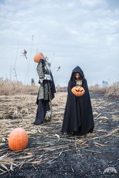 two people dressed as witches with pumpkins in the middle of an open field, one holding a jack - o - lantern