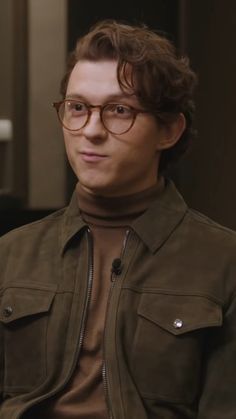 a man wearing glasses and a brown shirt is looking at the camera while sitting down