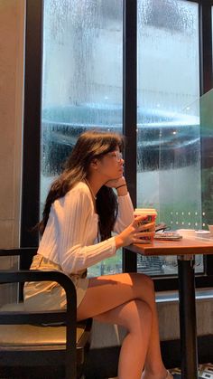 a woman sitting at a table with a cup of coffee in her hand and looking out the window