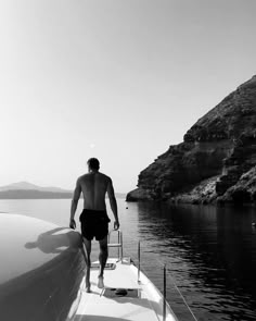 a man standing on the bow of a boat looking out at water and hills in the distance