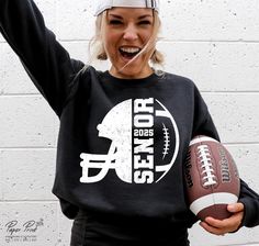 a woman holding a football in her right hand and wearing a black sweatshirt with the words san francisco on it