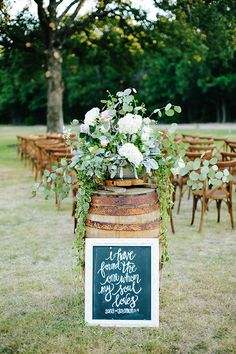 a wooden barrel with flowers and greenery on it is sitting in the middle of a field