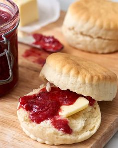 two biscuits with jam and butter are on a cutting board next to a jar of jelly