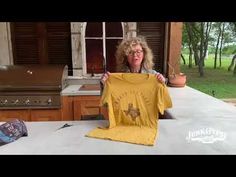 a woman holding up a yellow t - shirt in front of an outdoor bbq