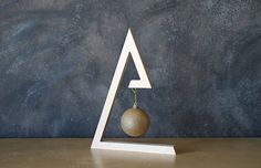 a white and gold sculpture with a ball hanging from it's side on a wooden table