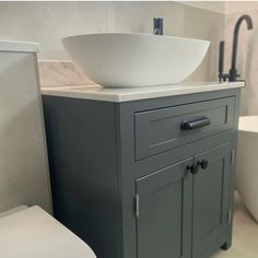 a white bowl sitting on top of a gray cabinet next to a toilet and sink