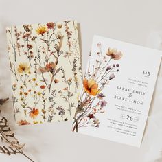 the wedding stationery is laid out next to some dried flowers and leaves on a white background