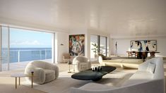 a living room filled with white furniture and large windows overlooking the ocean in front of it